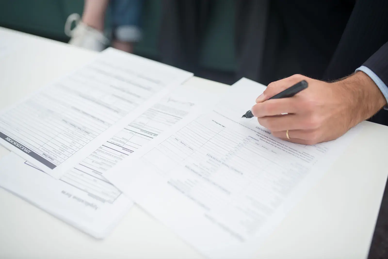 Hand in a suit sleeve signing printed forms on a white table